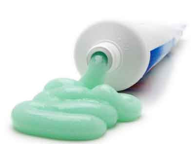 Tube of toothpaste with lots of green toothpaste curling out of the mouth