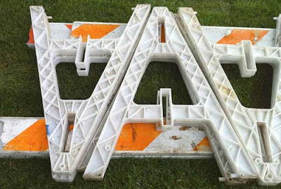 Orange and white caution sawhorses lying on grass, looking like a V and an A