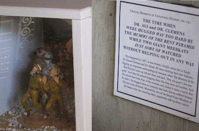 Small diorama of two human figures being choked by a mummy while two meerkats watch