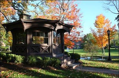 Brown Victorian gazebo on green grass with autumn leaves