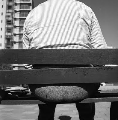 Photo of back of a park bench, showing a fat man sitting on it with his backside sticking out between the slats