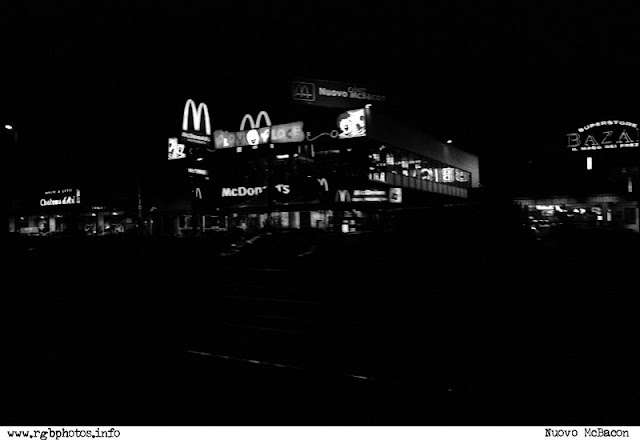 Fotografia notturna di un centro commerciale con le insegne del McDonald's.Macchina fotografica Canon EOS 50e, ottica Sigma 70-300mm f/4-5.6 APO, pellicola Kodak TMax 3200.