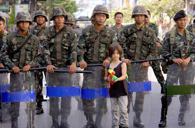 Seven year old boy Apple Rozas, from Britain, poses with a water gun for his father, in front of Thai soldiers after they cleared an intersection, in Bangkok, Thailand