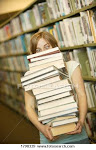 Young woman carrying a huge stack of books in a library
