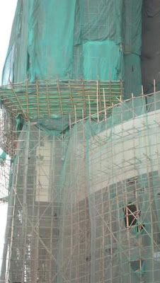 A more substantial bamboo scaffolding on a building site, with green mesh to prevent tools or material from falling out while allowing the wind to pass through with relative ease. Image of a more substantial bamboo scaffolding on a building site, with green mesh to prevent tools or material from falling out while allowing the wind to pass through with relative ease.