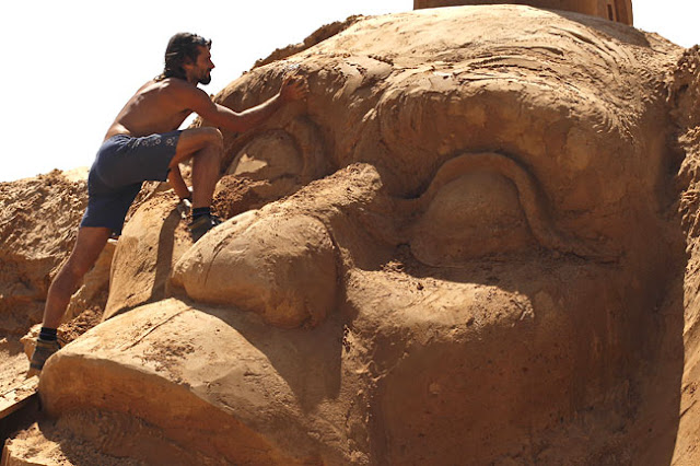 a man works on a sand sculpture of a primate