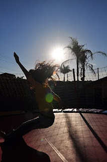 Sara em pleno salto no pula pula, com braços e cabelos pro ar, e o sol de fundo Sara em pleno salto no pula pula, com braços e cabelos pro ar, e o sol de fundo