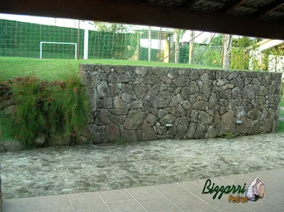 Muro de pedra construído com pedra moledo para formar o platô para a construção do campo de futebol com grama esmeralda.