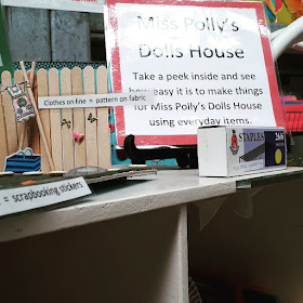 A variety of dolls' house decorating ideas displayed with signs explaining what they are made of. Next to them is a larger sign that says 'Miss Polly's Dolls House. Take a peek inside and see how easy it is to make things for Miss Polly's Dolls House using everyday items.
