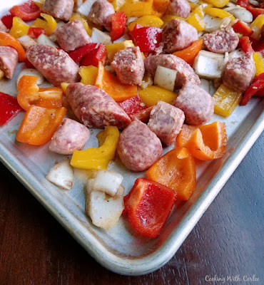 Italian sausage and peppers are a classic combination for a good reason: they are delicious together! Cooking them along with onions on a sheet pan makes it super easy. The clean up is really easy as well! Serve the mixture over pasta or rice for a fabulously quick meal. chunks of raw onion peppers and sausage on sheet pan ready to cook