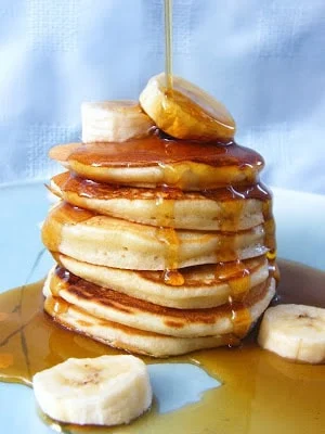 A stack of Scotch pancakes drizzled with maple syrup and served with sliced banana on a blue plate