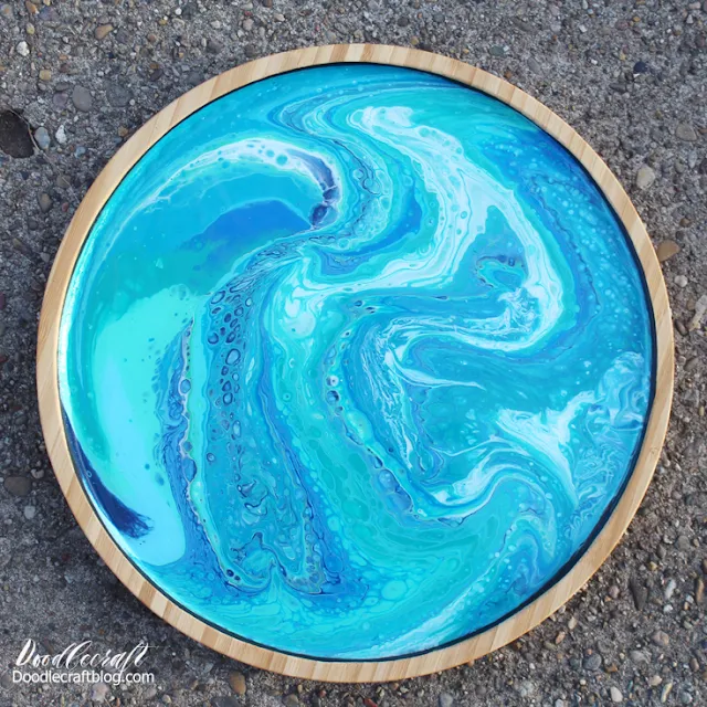 Using shades of blue paint to pour swirls and cells on a round bamboo serving tray, coated in high gloss resin.