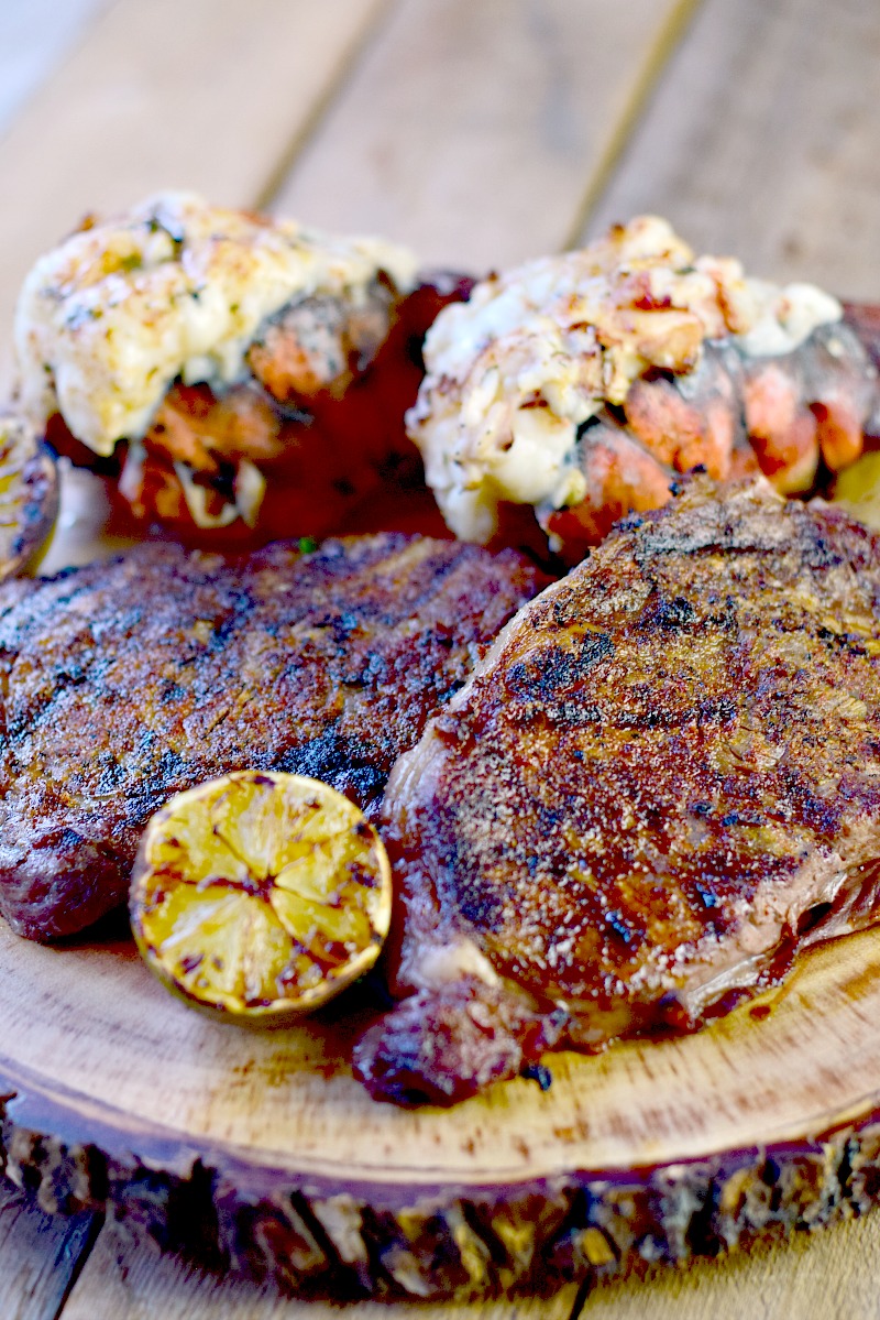 Grilled Mexican Style Surf and Turf with grilled lime halves on a round wooden board.