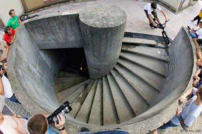 A GIF of a teen boy BMXer riding a bike down a spiral set of stairs.