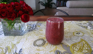 a glass filled with smoothie on a table with some flowers