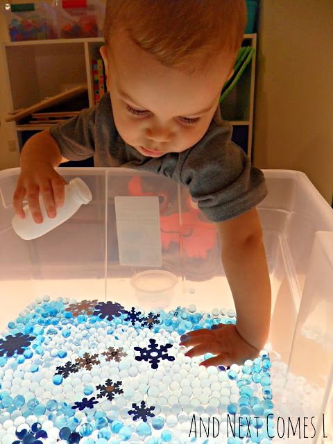 Toddler playing with a winter themed water beads sensory bin on a light table