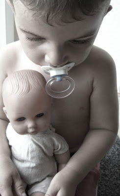 Kind nuckelt mit Puppe auf dem Schoß