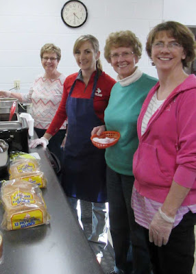 four women smiling for camera at station with hamburger buns and condiments