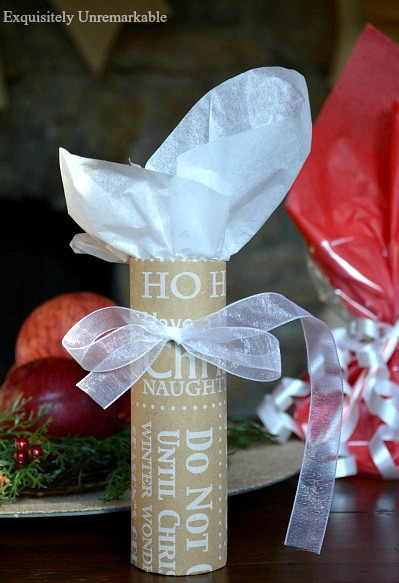 Christmas paper wrapped around toilet paper tube and tied with white ribbon