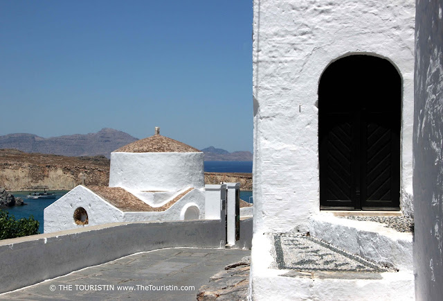 A travel guide to Lindos in Greece. The Touristin A path between the entrance of a white cubic house and a white small church.