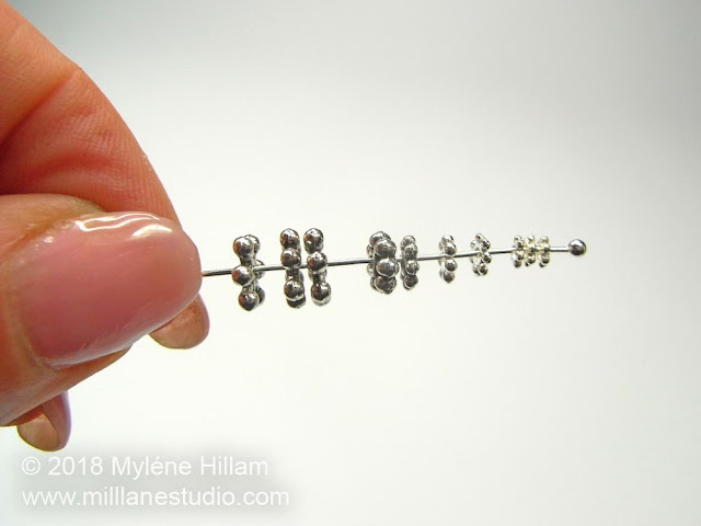 A stack of silver daisy spacers in graduating sizes strung on a head pin.