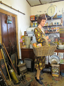 Full-scale model of the interior of a 1930s shop, with a customer with a basket on her arm.