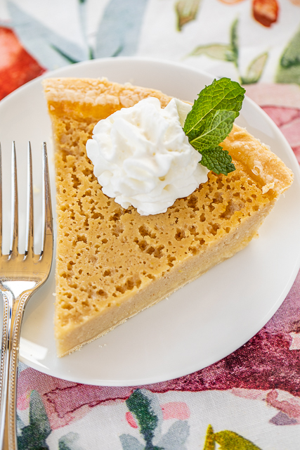 Sweet Tea Buttermilk Pie - two Southern favorites in one classic dessert. SO good!! I don't even like sweet tea and I LOVED this pie!! Super easy to make. Infuse buttermilk with tea bags and then whisk in sugar, lemon zest, eggs, butter, flour and vanilla. Bake in a frozen pie crust. Can make in advance and freeze for a quick dessert later. A MUST for all your cookouts and potlucks! #pie #dessert #buttermilkpie slice of pie topped with whipped cream and mint