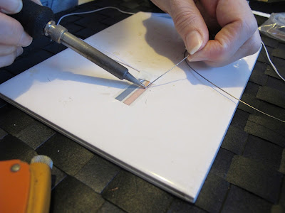 Woman adding flux to length of wire on a run of copper tape.