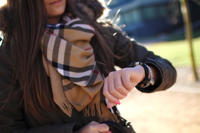 Person in brown coat and tartan scarf checking the time on their watch