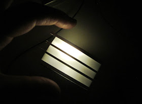 Modern dolls' house miniature light box, half built but lit up, with hand for size reference.
