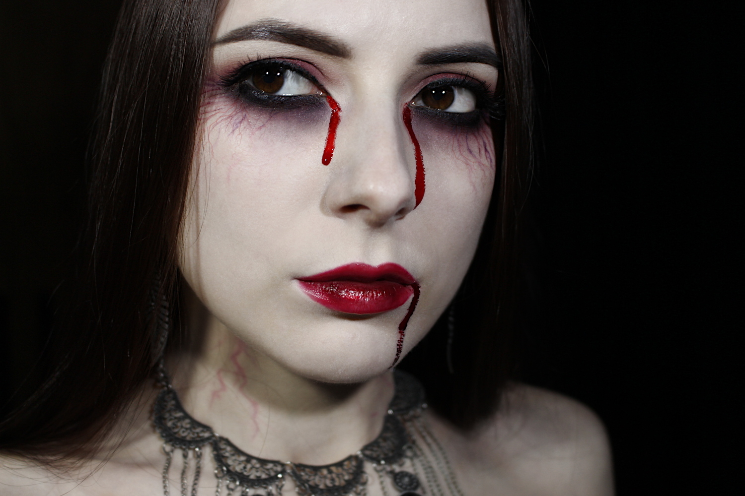 a close-up of Liz Breygel's face with a dramatic vampire makeup look and false blood tears for Halloween