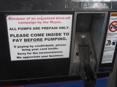 Gas pump with this sign attached: Because of an organized drive-off campaign by the Mayor, all pumps are prepaid only. Please come inside to pay BEFORE pumping.