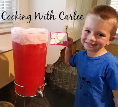 little guy holding pink ink drink sign by large drink dispenser filled with pink punch