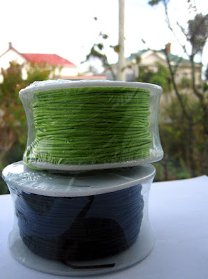 Two packages of waxed thread, one lime green and one black.