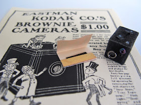 1/12-scale vintage box brownie camera and photo packet, on a full-sized advertisement for the camera.