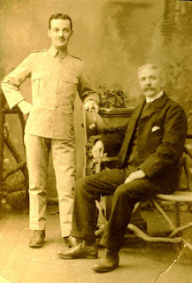 Studio portrait of two men, one standing in military uniform, the other, older sitting.