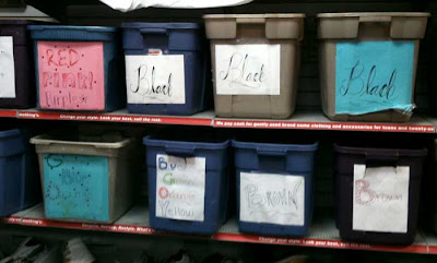 Gray bins on a shelf with hand-drawn cursive color names like Black, Red