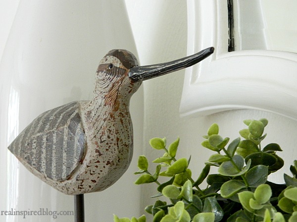 A fresh spring mantel decorated using plants, bird, and feathers and set against alabaster white walls. 
