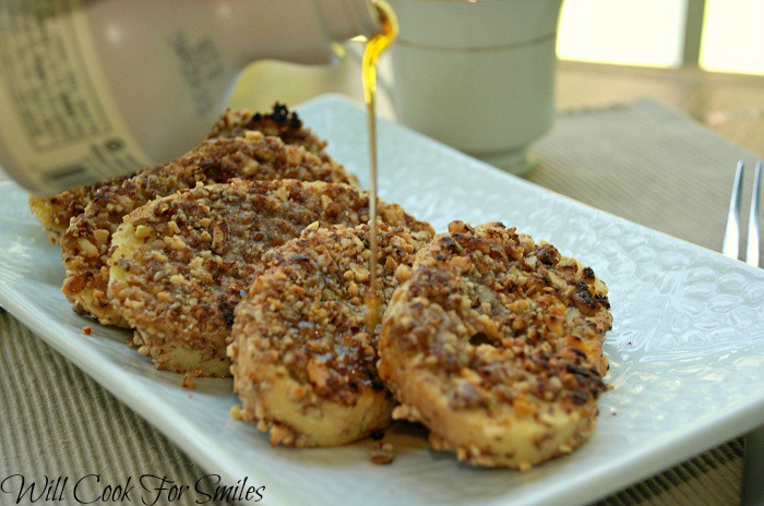 5 slices of pecan crusted french toast with syrup being poured over them on a white platter 