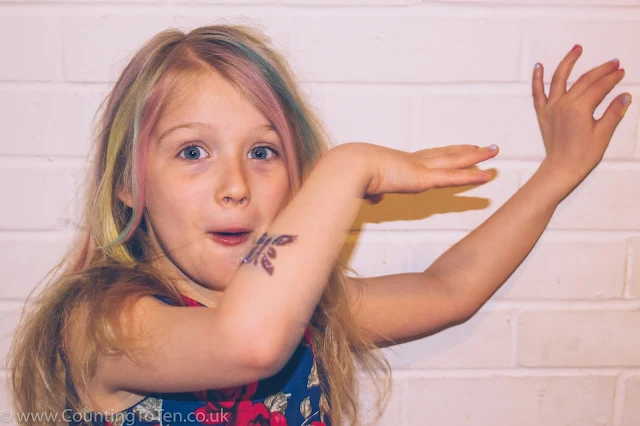 A young girl doing a silly pose to show off her nail polish, glitter tattoo and coloured hair