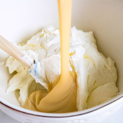 pouring sweetened condensed milk over bowl of whipped cream