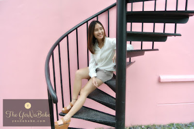 She sits on the staircase looking to her left with the pink wall behind her at Once Upon A Time Cafe Johor Bahru