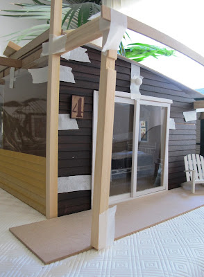 Dry fit of a dolls' house shed kit, with stained weatherboarding taped to the sides and pergola posts and struts taped in place.