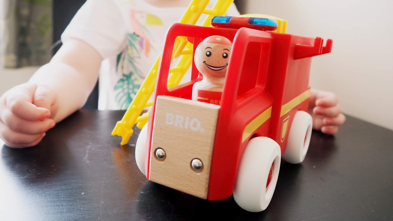 A close up photo of the fire truck toy. The brio logo can be seen on the front, with a wooden man inside the front of the fire truck. Elise is sitting behind.