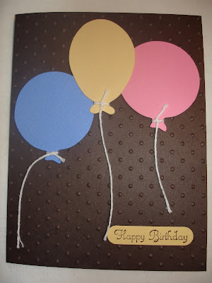 Brown card embossed with polka dots and three die-cut balloons (pink, yellow and blue).