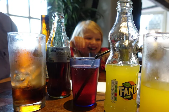 Bottles of soft drink including fanta, diet coke and blackcurrant squash and a young girl grinning in the background