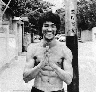 [bruce lee che saluta tenendo le mani unite, con il torso nudo]