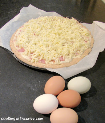 getting ready to put eggs on pizza pizza crust covered with creamy sauce, ham and cheese with eggs nearby