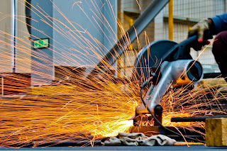 Stock photo of an angle grinder being used to cut steel, producing a fan of gold and orange sparks.