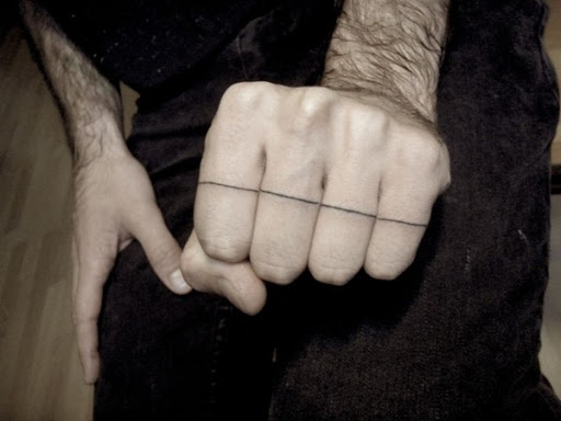 Uma fina linha preta é executado ao longo de todos os quatro dedos sobre o portador da mão esquerda essa tatuagem.
